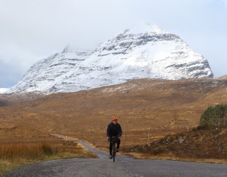 Cyclist cycling the North Coast 500 with snow on the mountains behind